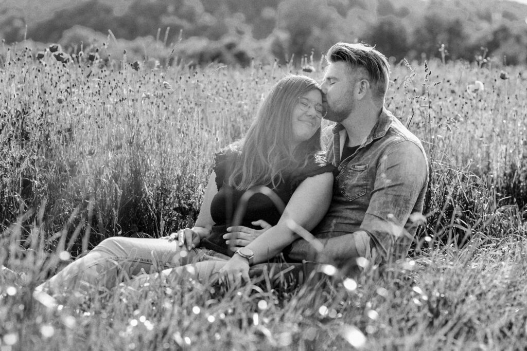 Fotograf Reutlingen Tübingen Hochzeit Paar sitzen in einem Mohnblumenfeld und er küsst ihre Stirn in Tübingen