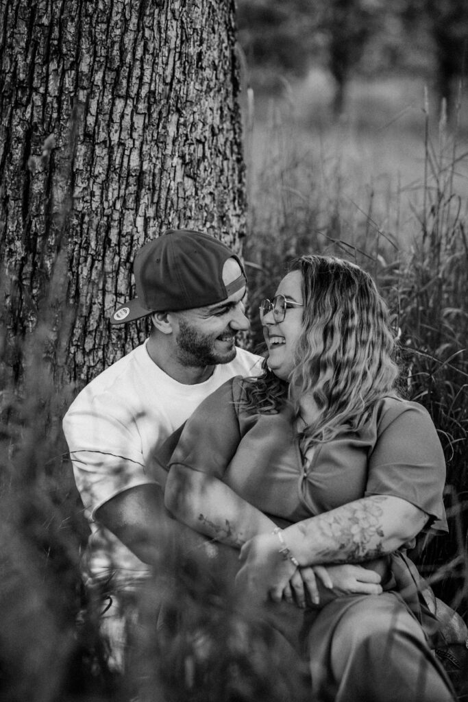 Fotograf Reutlingen Tübingen Hochzeit Paar sitzt in einer Wiese an einem Baum und lacht sich an in Pliezhausen